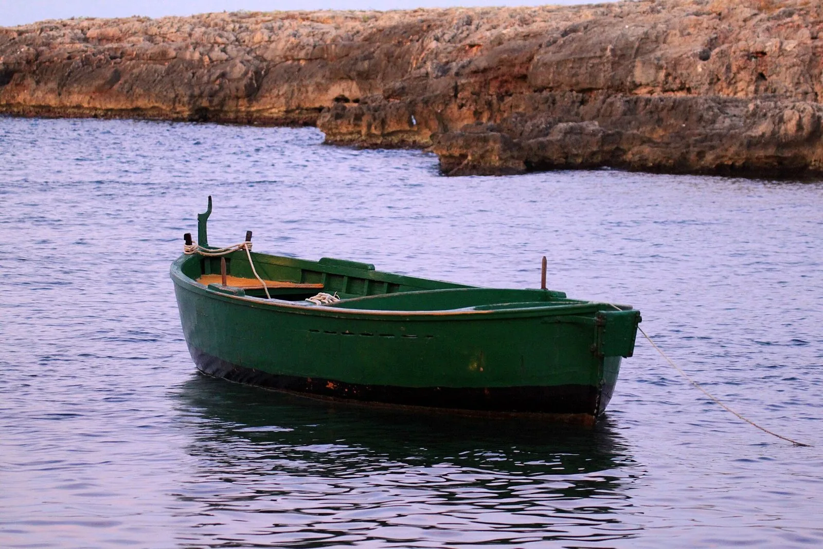Barca di pescatori verde ormeggiata in una cala di roccia sulla costa adriatica